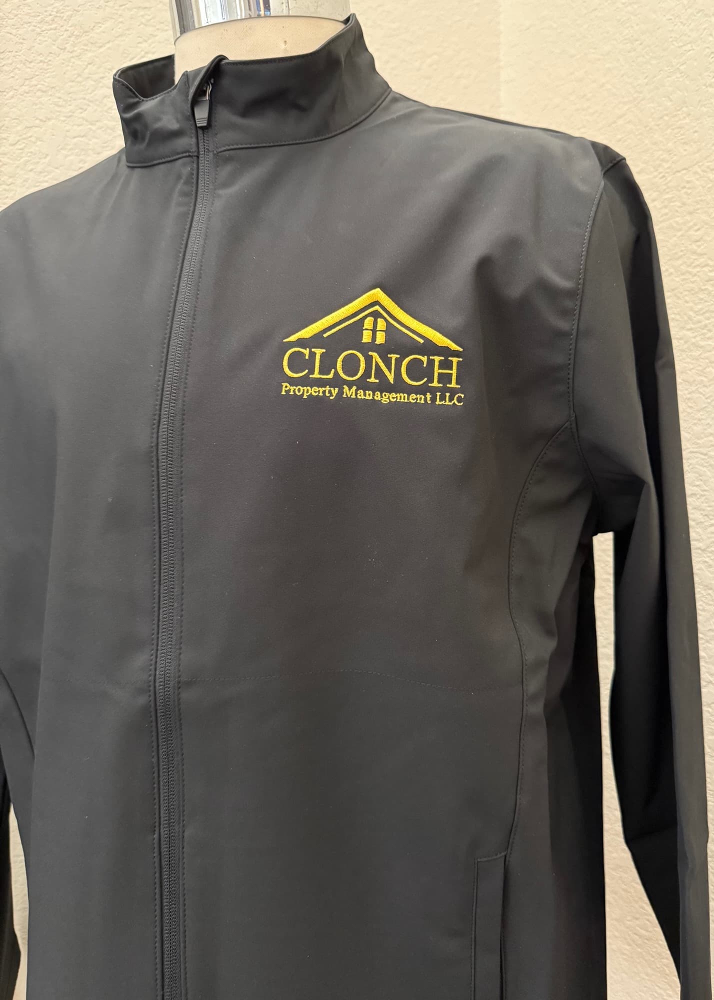 Black soft-shell jacket embroidered with the gold Clonch Property Management logo