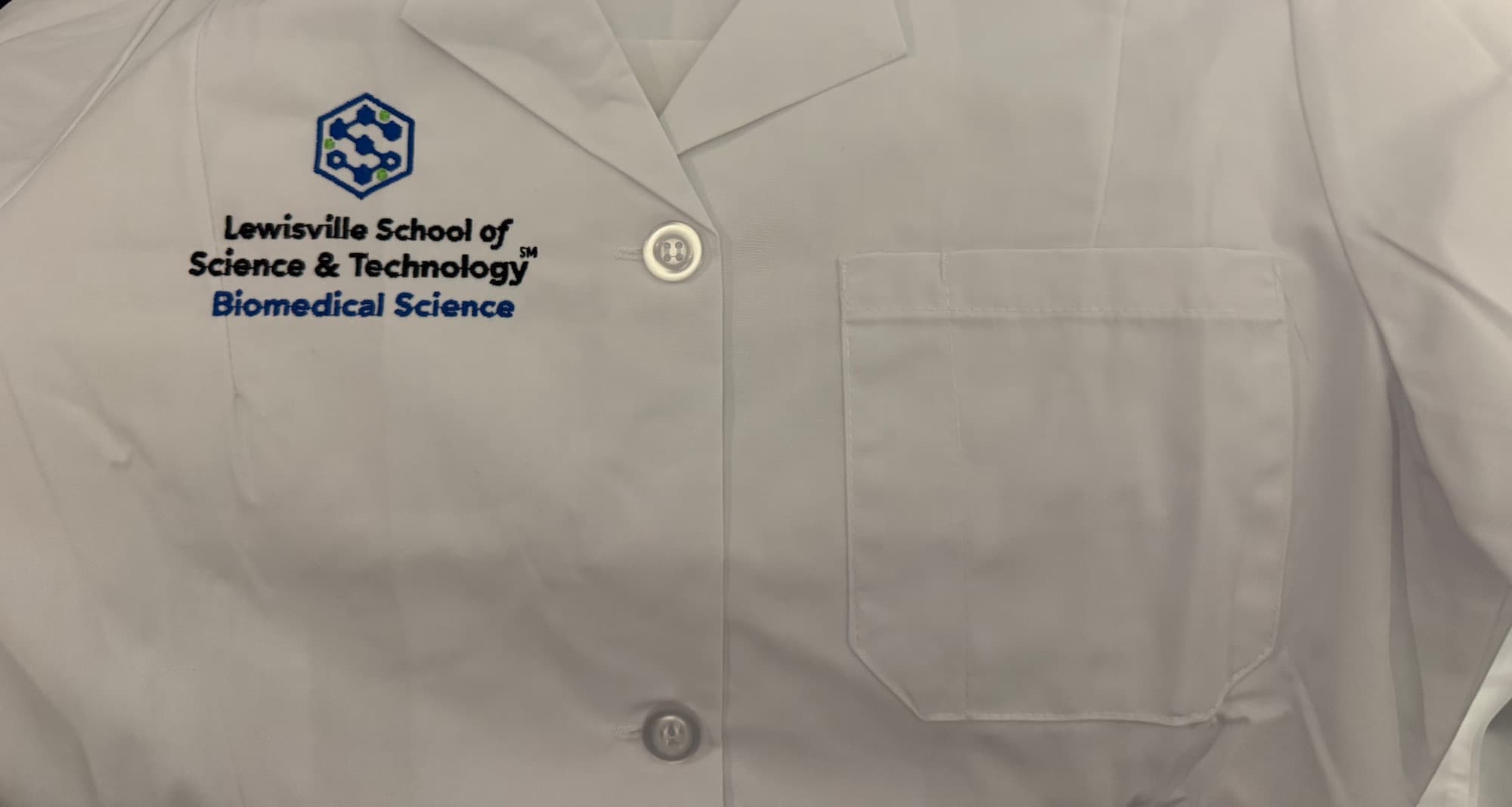 White lab coat embroidered with the Lewisville School of Science & Technology Biomedical Science logo